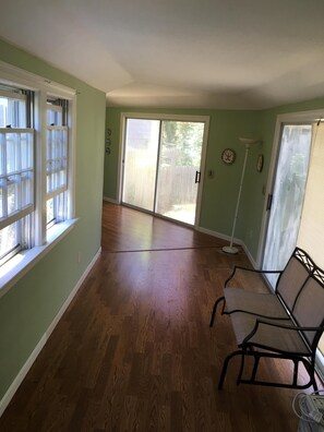 Amplia habitación con un gran ventanal corredero que da a un patio, una ventana con persianas y una silla cerca de la puerta.