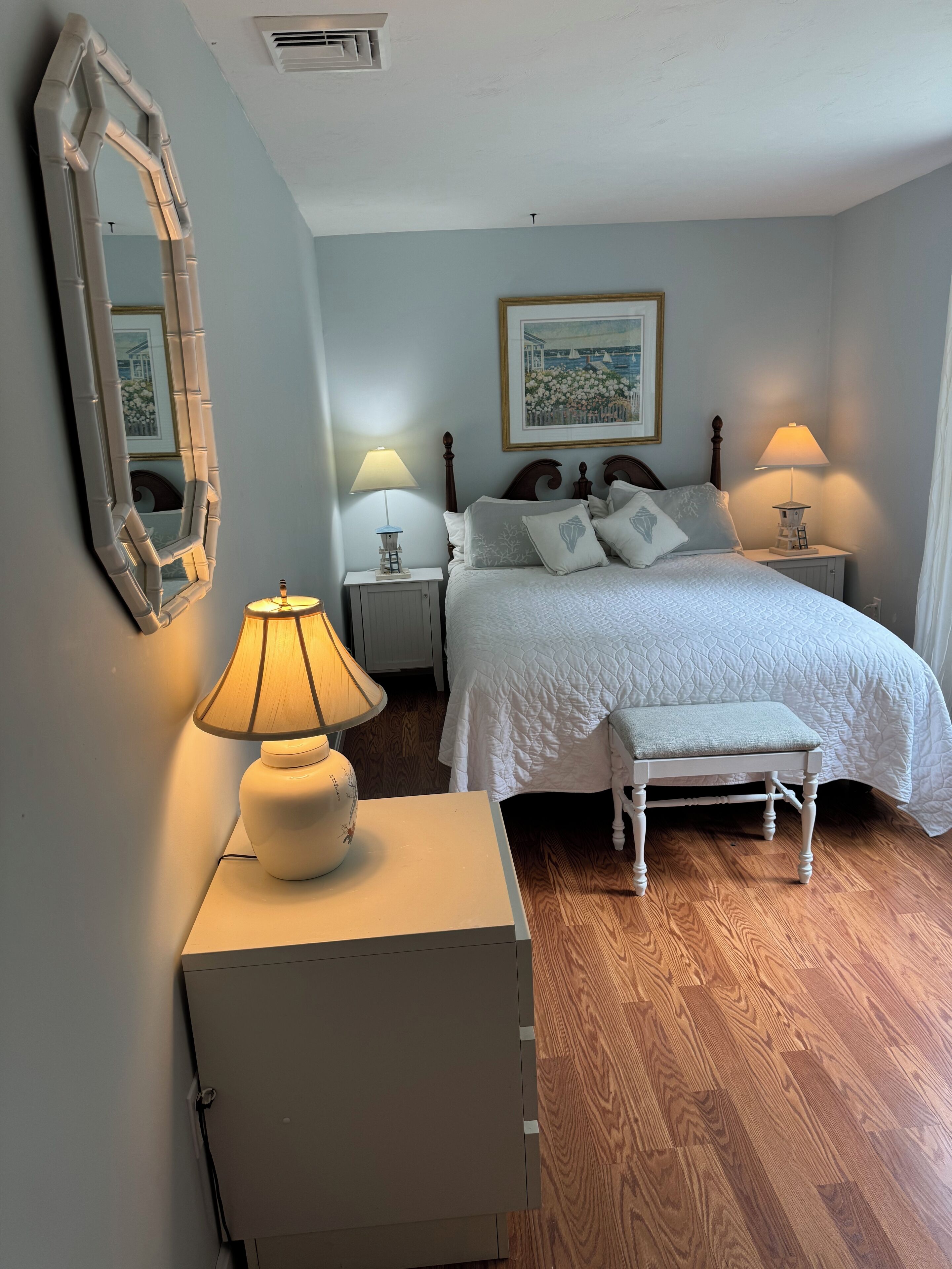 Ein Schlafzimmer mit einem Bett, Nachttischlampen, einem Spiegel, einer Bank und einem Schrank.