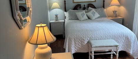 A bedroom with a bed, bedside lamps, a mirror, a bench, and a cabinet.