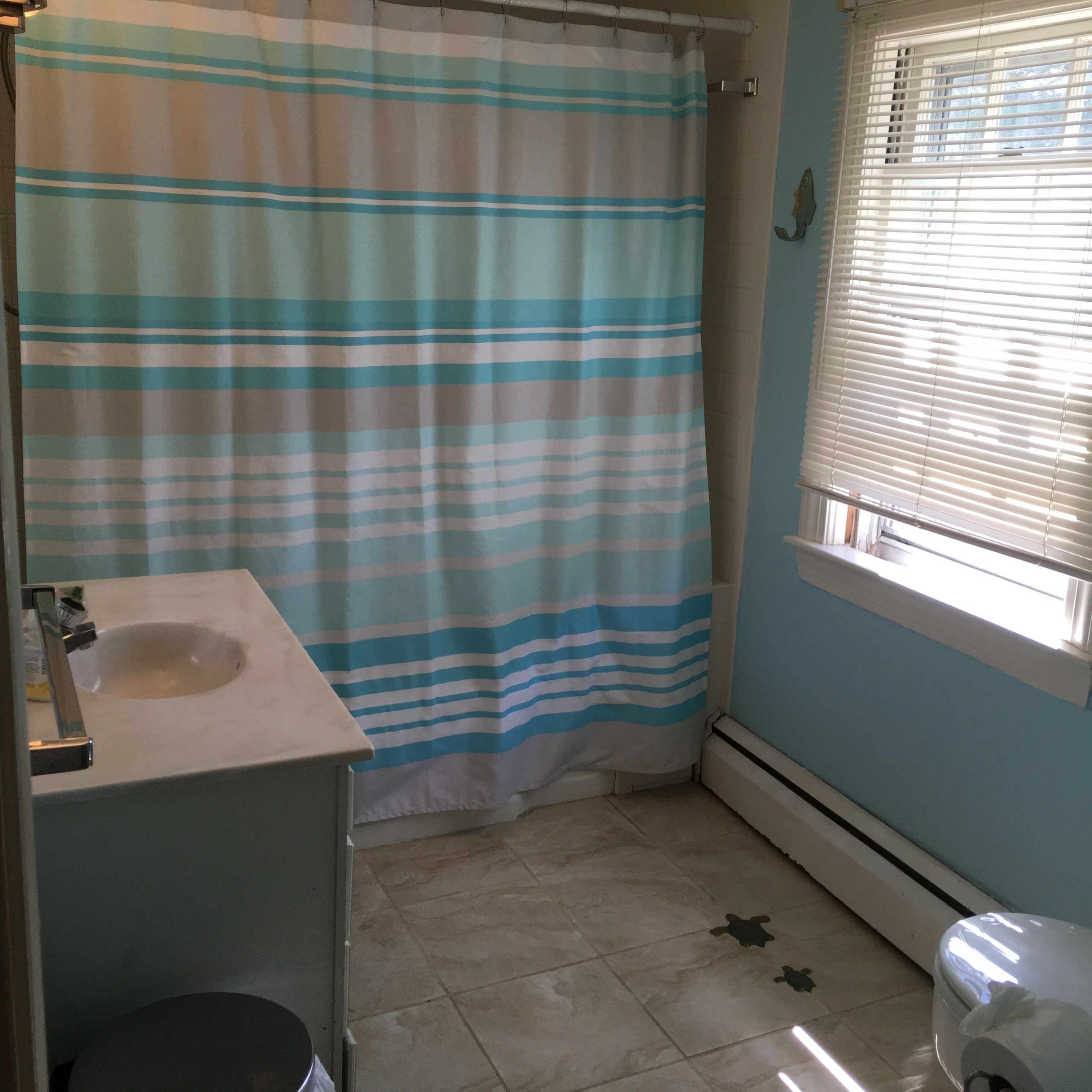 Un baño con cortina de ducha a rayas, un lavamanos y una ventana con persianas.
