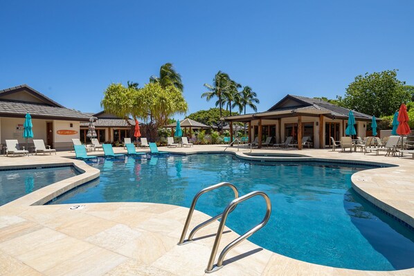 A pool area with lounge chairs and umbrellas, surrounded by buildings with a tropical theme.