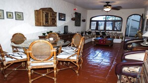 Ein geräumiges Wohnzimmer mit Essbereich, ausgestattet mit Korbmöbeln, einer Holzeinrichtung und einem großen Fenster mit Jalousien.