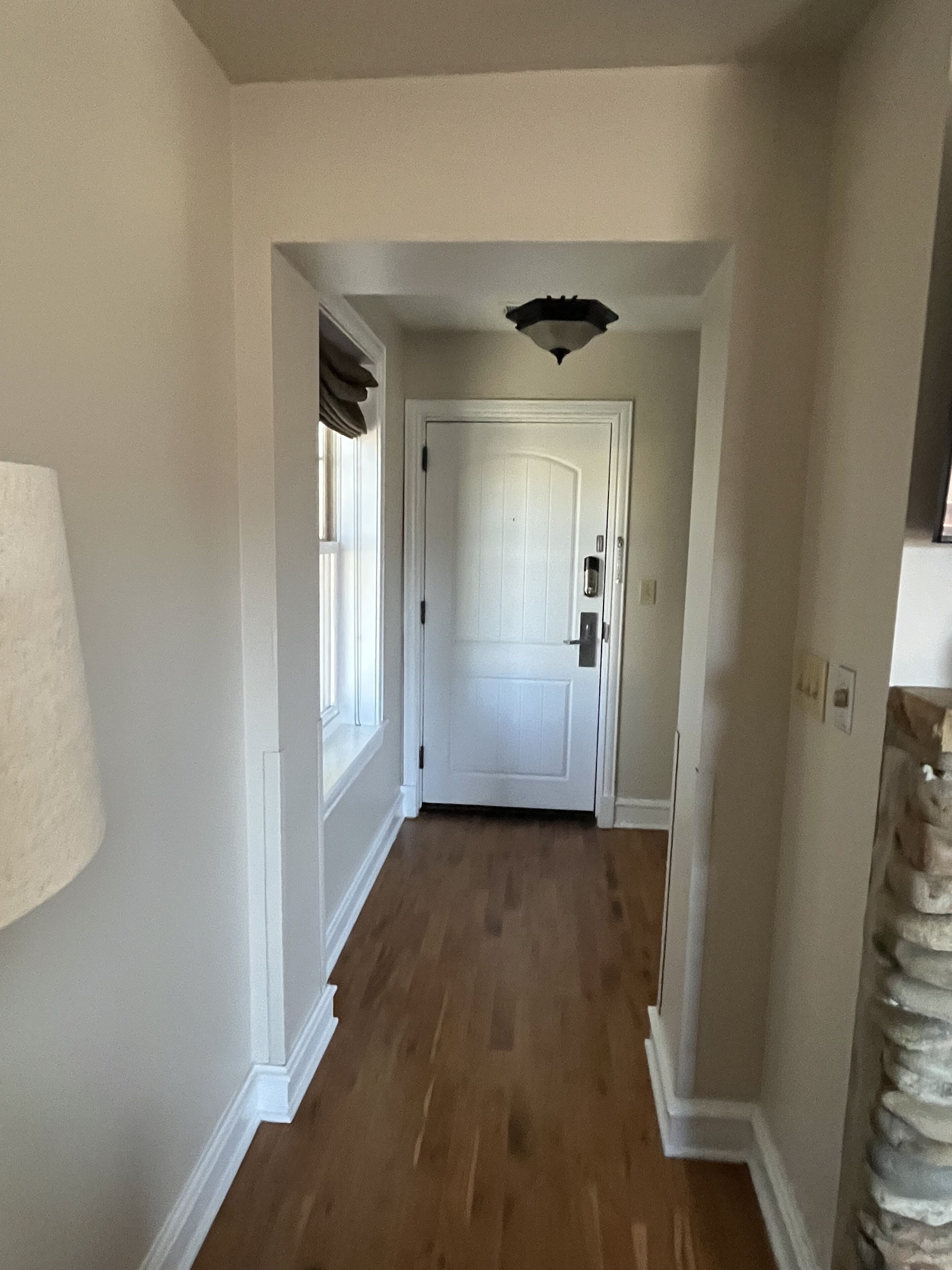Un couloir doté d’un plancher en bois, de murs blancs et d’une porte blanche au fond.