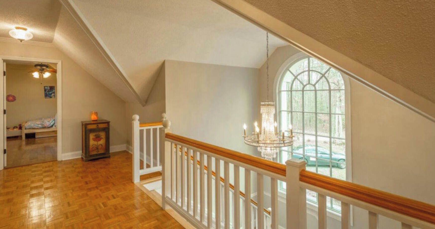 A staircase with white railings and a chandelier, leading to a room with a large window and a door.