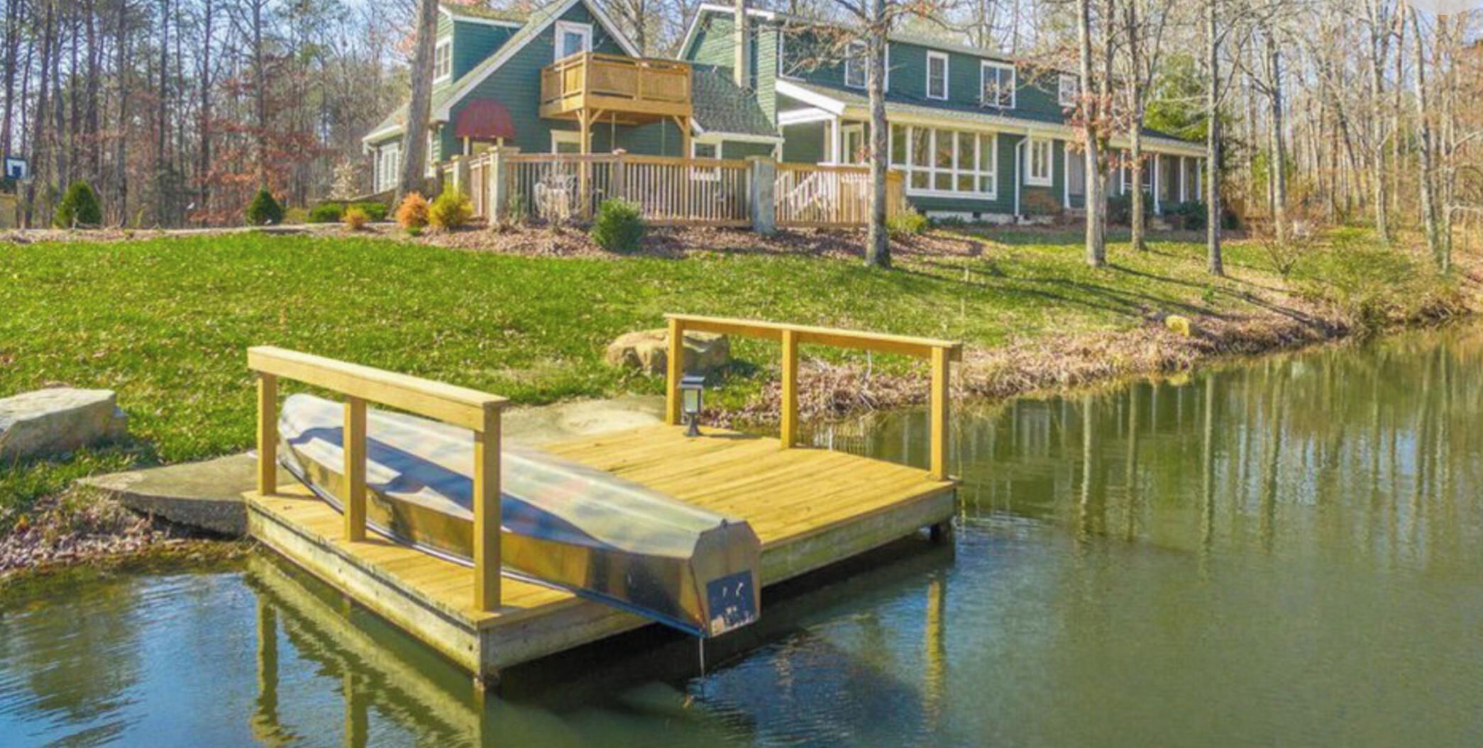 A wooden dock extending into a calm body of water, with a house in the background.