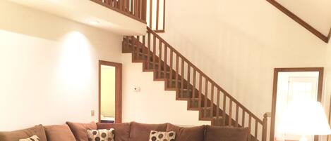 A living room with a brown sectional sofa, a wooden staircase, and a ceiling fan.