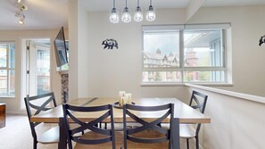 A dining area with a wooden table and black chairs, a large window with a view of buildings, and a ceiling light fixture.