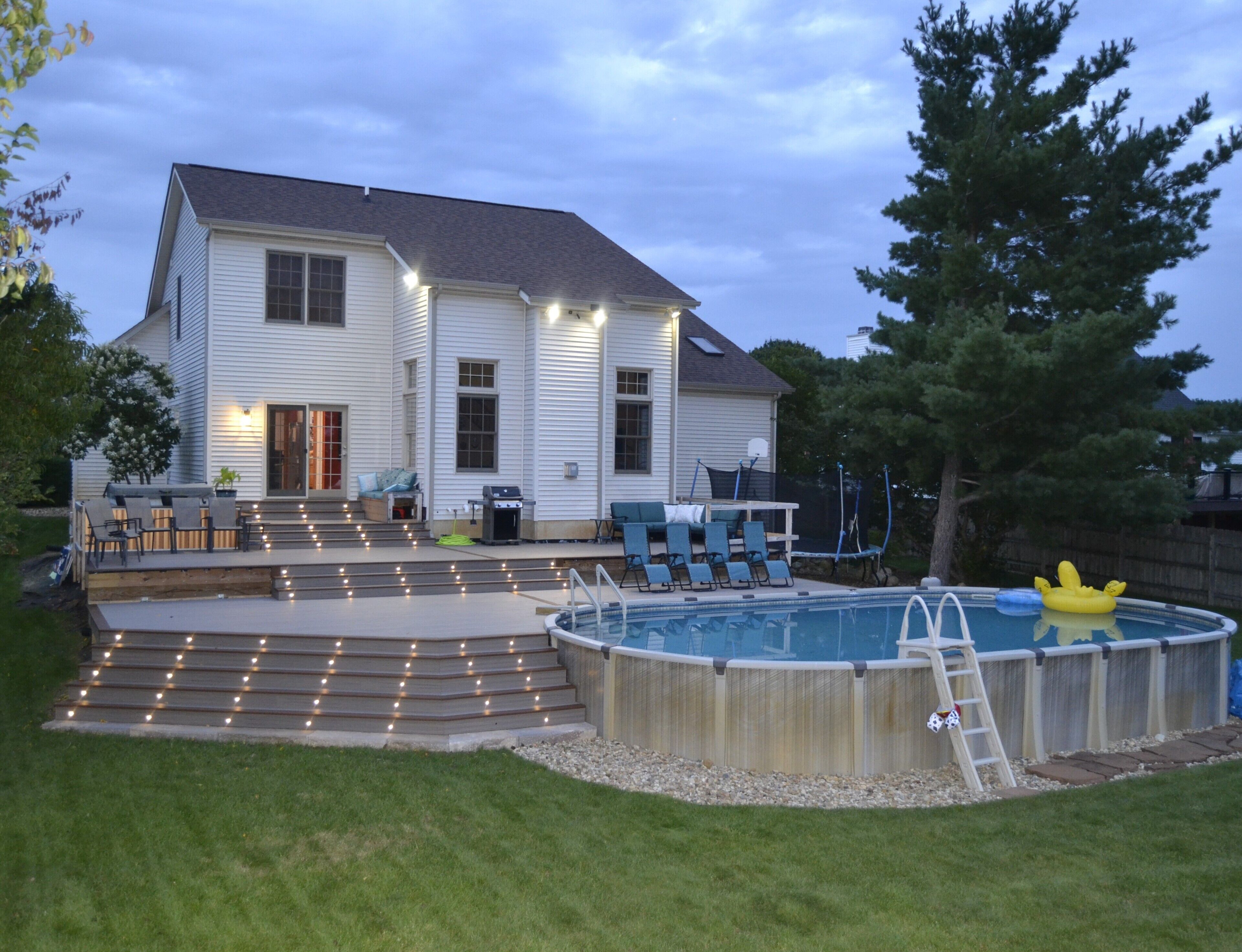 Una casa de dos pisos con un deck en el patio trasero, una piscina y mobiliario exterior.