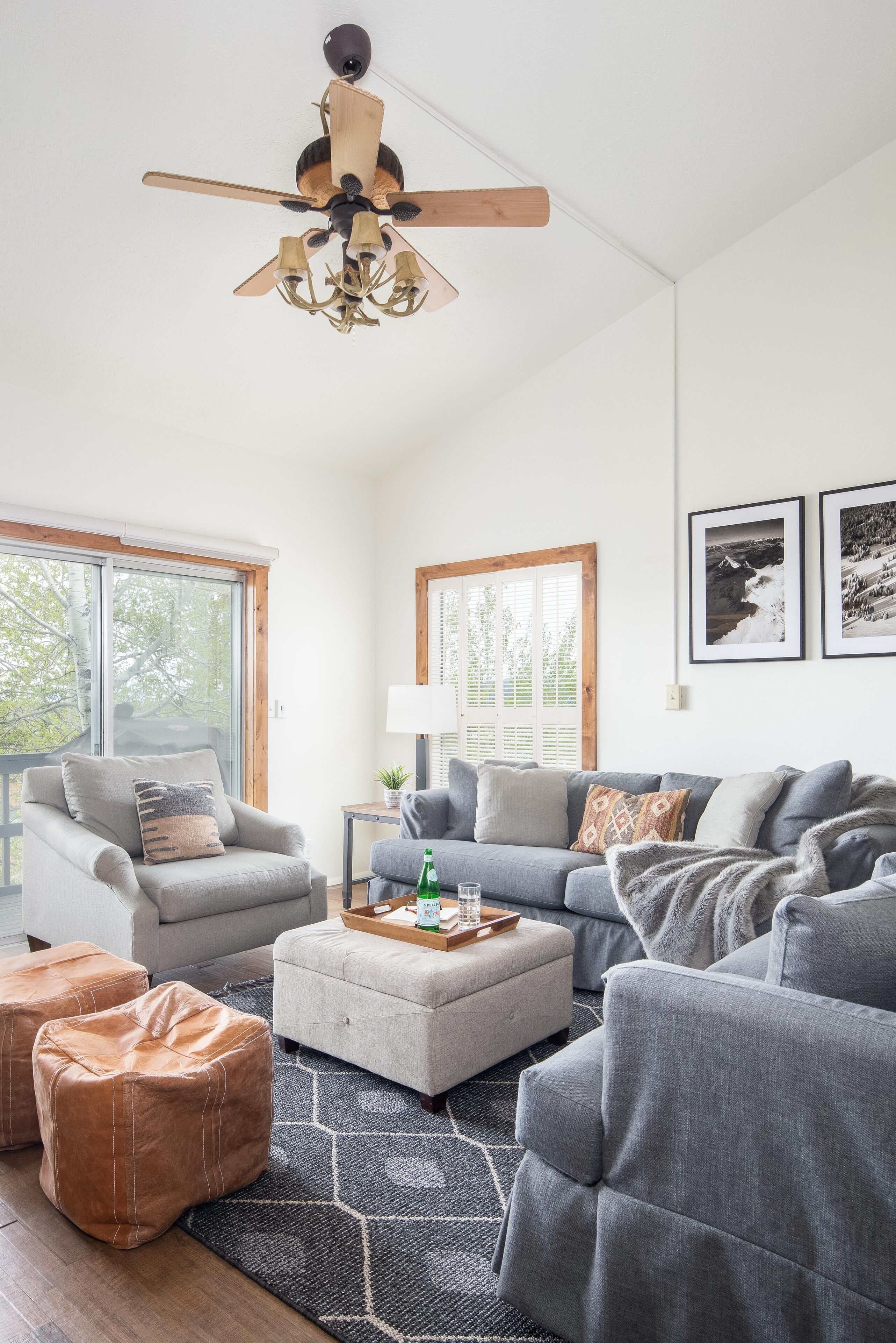 Un salon moderne avec un ventilateur de plafond, des canapés gris, une table basse et une grande fenêtre.