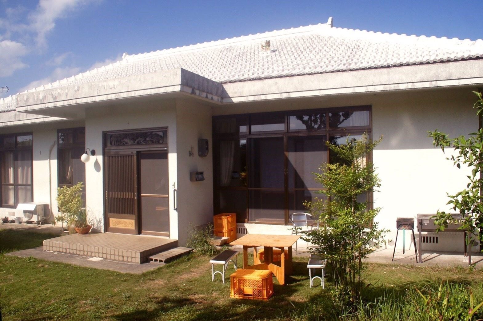 A modern house with a large glass door, a small patio with a table and chairs, and a garden area.