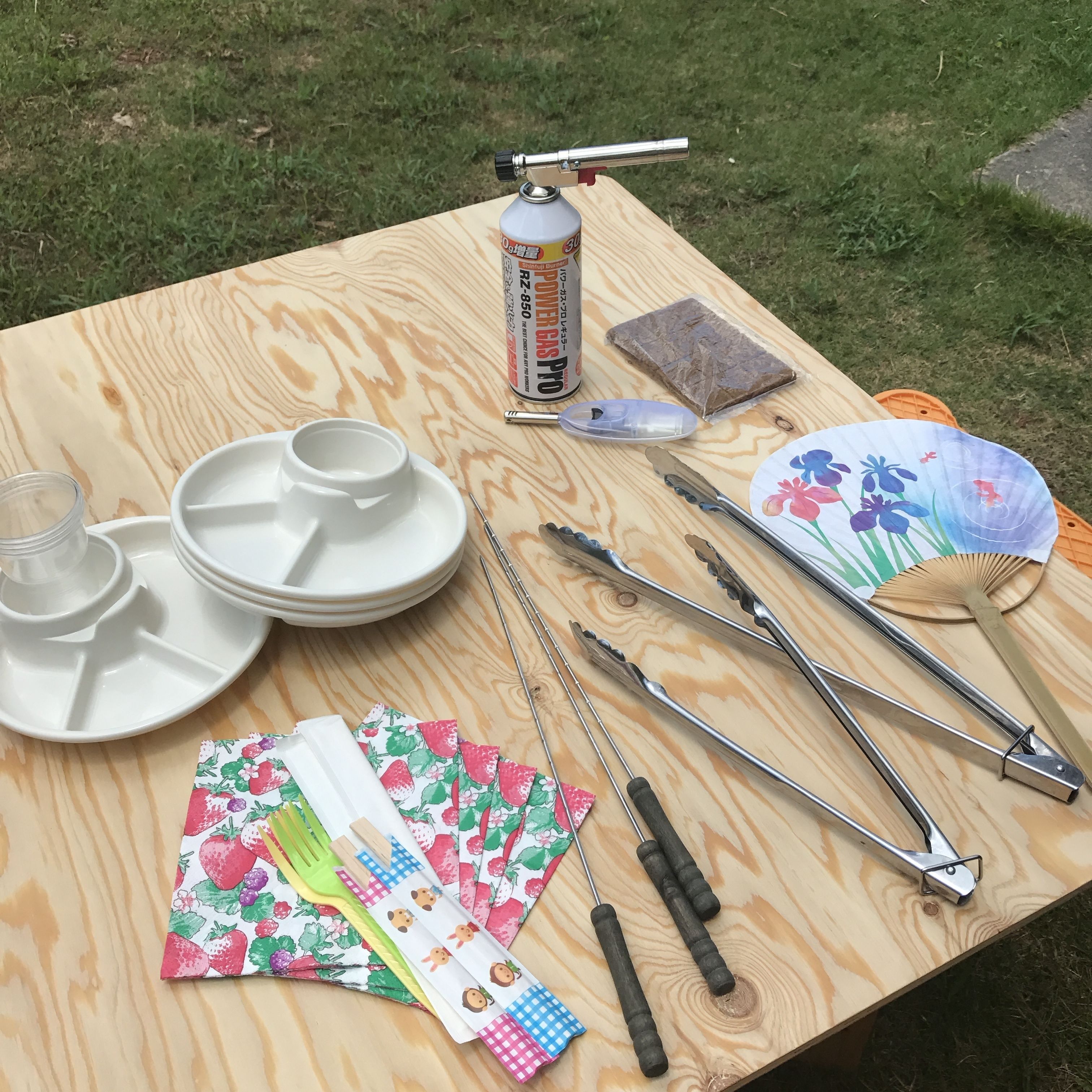 Une table en bois sur laquelle on trouve divers ustensiles de cuisine, des assiettes, un récipient et un ventilateur.