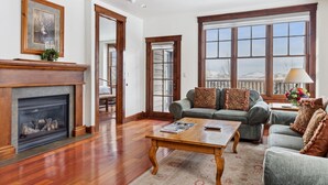 A spacious living room with a fireplace, a sofa set, and large windows offering a view.