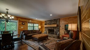 A cozy log cabin interior with a fireplace, wooden walls, a dining area, and a comfortable seating arrangement. - LAKEFRONT, PONTOON BOAT, HOT TUB, FIREPIT, Fireplace . Wide lake Mountain View  (Blairsville)