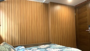 A bedroom with a wooden slatted wall, a bed with a floral bedspread, and a wooden door. - HK Mingdu Hostel (Kowloon)