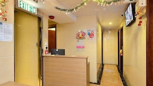 A hotel reception area with a wooden reception desk, an exit sign, and a wall-mounted television. - HK Mingdu Hostel (Kowloon)