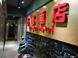 A hotel entrance with a Christmas tree and a sign in both Chinese and English. - HK Mingdu Hostel (Kowloon)