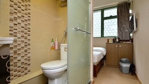 A compact bathroom with a toilet, shower, and a small bed area. - HK Mingdu Hostel (Kowloon)