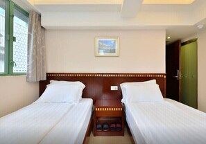 A hotel room with two single beds, a wooden headboard, a small table with shoes, a framed picture on the wall, and a window with curtains. - HK Mingdu Hostel (Kowloon)
