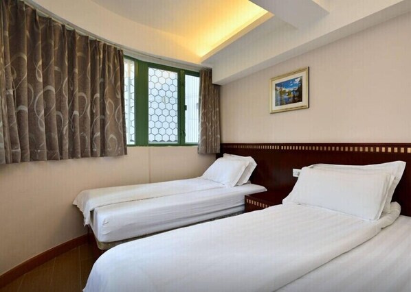 A hotel room with two single beds, a window with curtains, a painting on the wall, and a wooden headboard. - HK Mingdu Hostel (Kowloon)