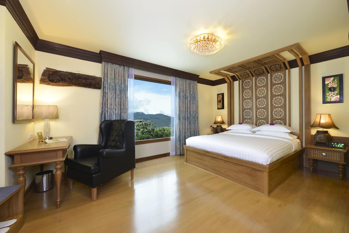 A hotel room with a large bed, a desk, a chair, a nightstand, and a view of the outdoors.
