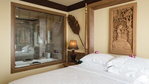 Une chambre d’hôtel avec un grand lit, une table de chevet avec une lampe, un grand miroir et une sculpture décorative sur le mur.