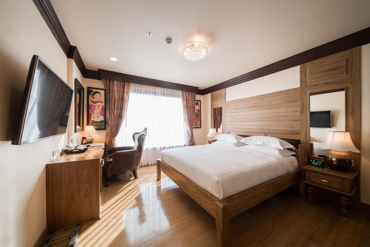 A hotel room with a wooden bed, a desk, a chair, a TV, and a nightstand with a lamp.