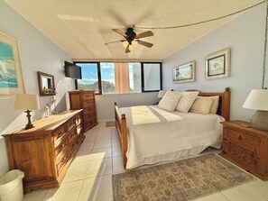 A bedroom with a bed, wooden dresser, nightstands, a ceiling fan, and a window with curtains.