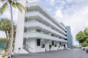 A multi-story building with a modern architectural design, featuring balconies and a parking area.