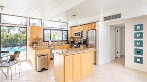 A modern kitchen with a central island, wooden cabinets, stainless steel appliances, and a view of a swimming pool. - Desert Modern by Jack Meiselman with Pool/Spa (Palm Springs)
