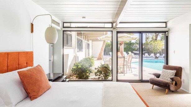 A modern bedroom with a large bed, a view of a pool and outdoor seating, and a sliding glass door to the outside. - Desert Modern by Jack Meiselman with Pool/Spa (Palm Springs)
