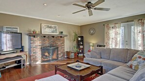 A living room with a brick fireplace, a ceiling fan, a television, a sofa, and a coffee table.