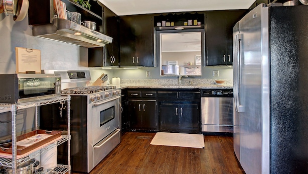 A modern kitchen with stainless steel appliances, dark cabinetry, and a wooden floor.