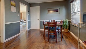 A dining area with a wooden table and chairs, a potted plant, and a framed picture on the wall.
