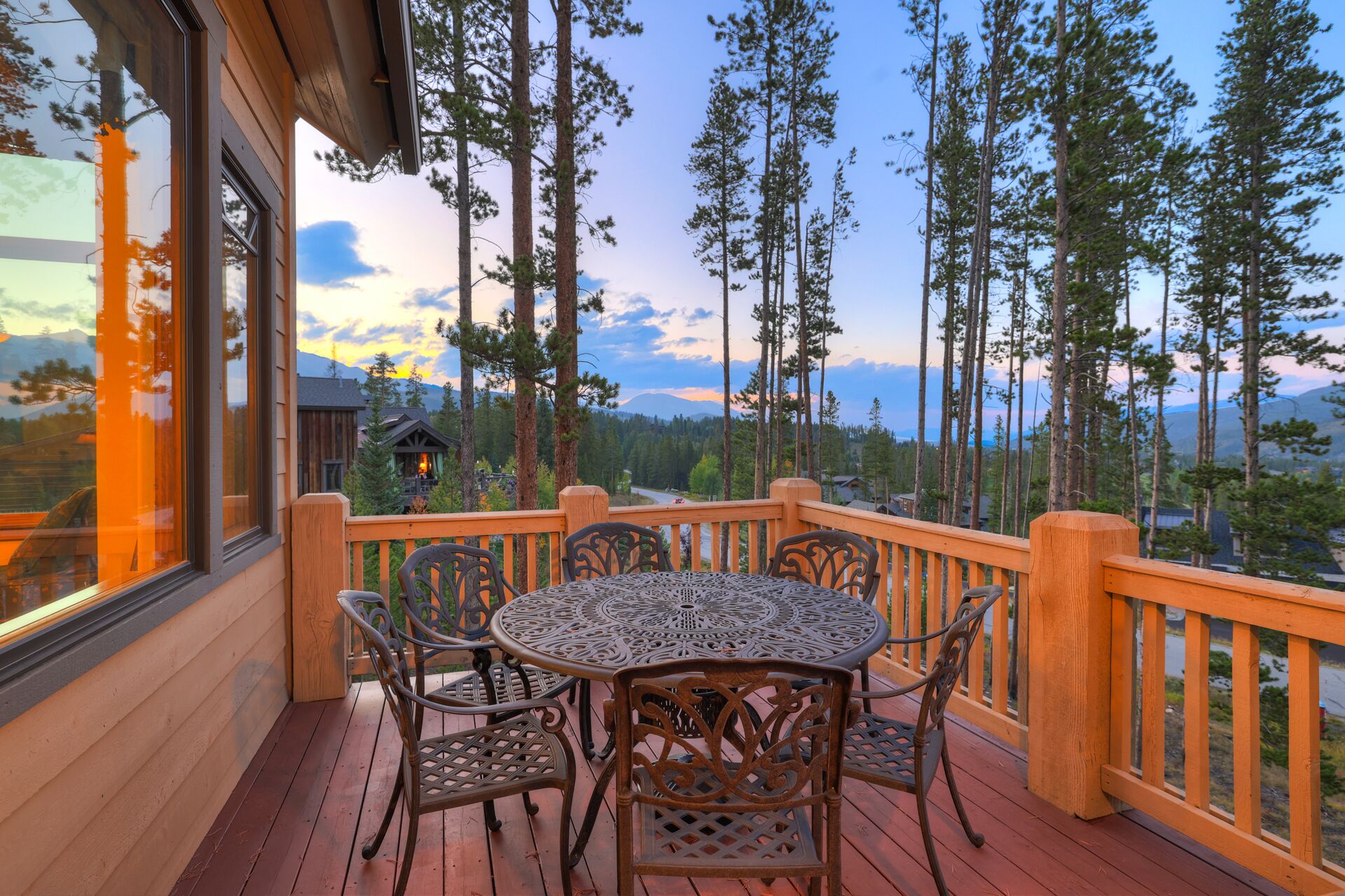Une terrasse en bois avec une table ronde et des chaises, d’où l’on a vue sur une forêt et des montagnes.