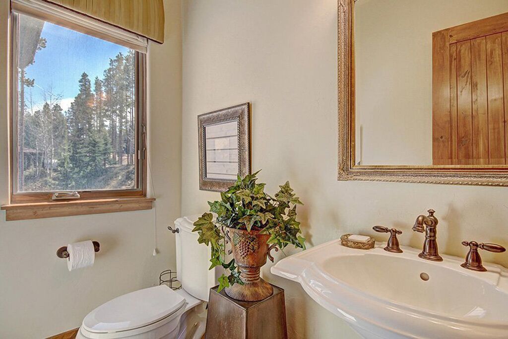 Une salle de bain équipée de toilettes, d’un lavabo et d’une fenêtre donnant sur des arbres.