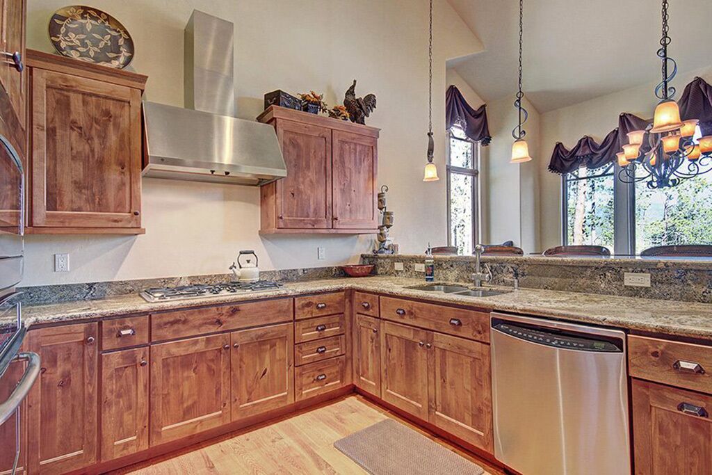 A kitchen with wooden cabinets, a stainless steel range hood, a dishwasher, and pendant lighting.