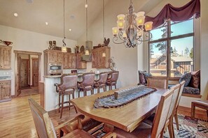 Un comedor amplio con una mesa y sillas de madera, una araña y vistas al exterior.