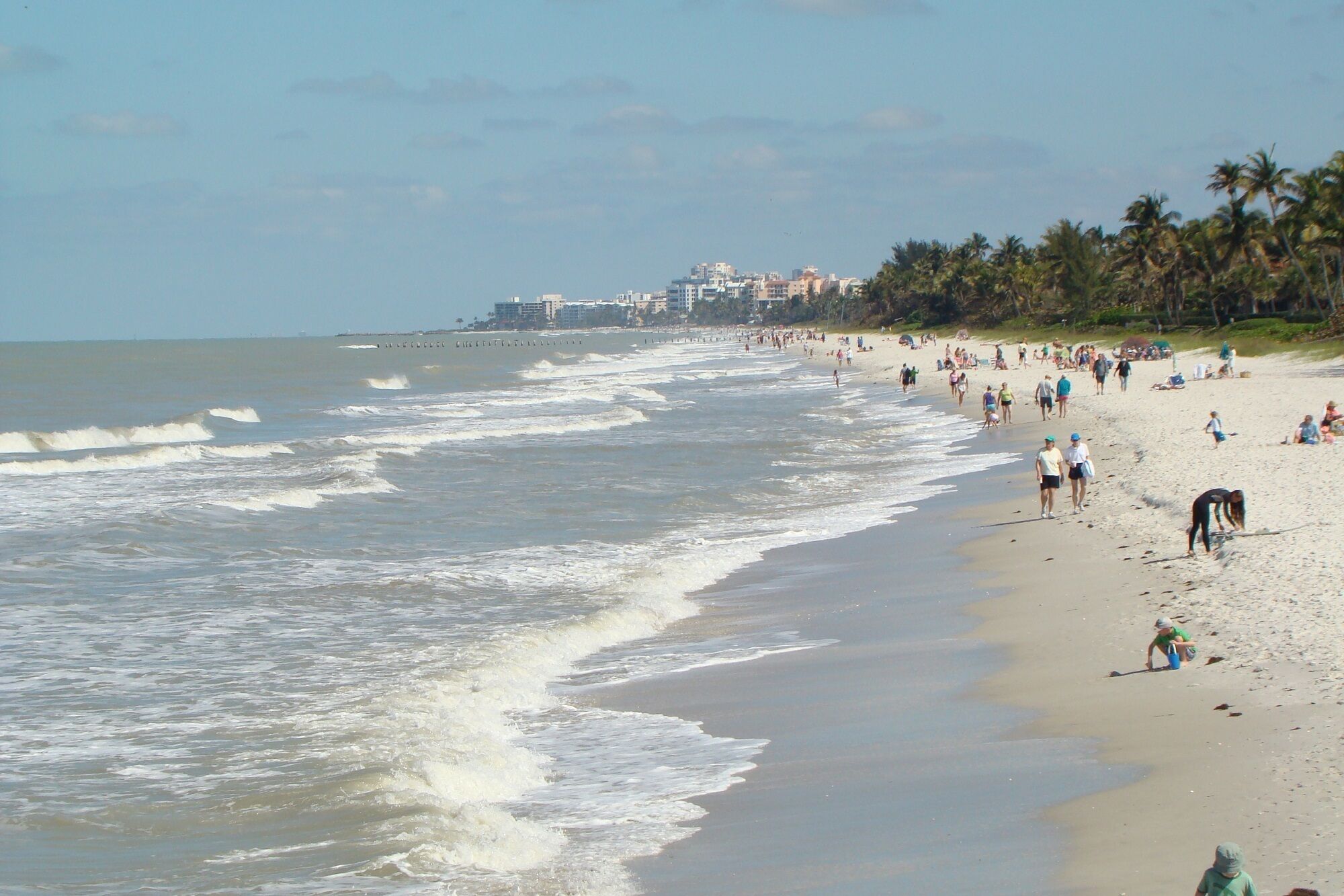 A beach with waves, people, and buildings in the background.