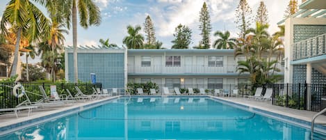 A swimming pool with lounge chairs and palm trees, surrounded by a building with a patterned facade.