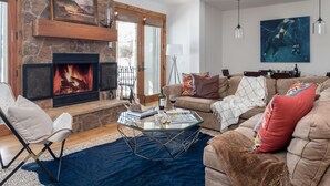 A living room with a stone fireplace, a glass coffee table, a sofa, and a painting on the wall. - Outpost: Granite Canyon at Teton Pines (Wilson)
