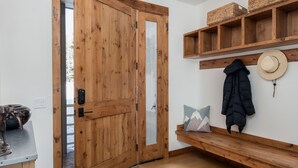 A wooden door with a glass panel, a bench with baskets, a hat, and a coat hanging on the wall. - Outpost: Granite Canyon at Teton Pines (Wilson)