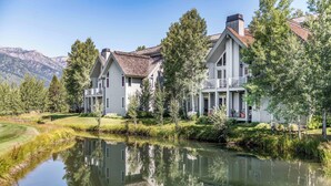 A two-story house with a balcony, a pond in front, and mountains in the background. - Outpost: Granite Canyon at Teton Pines (Wilson)