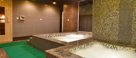 Un área de spa con dos jacuzzis, una puerta de madera y una pared de azulejos.