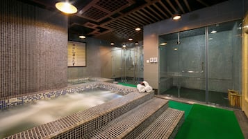 Relax in a spacious hot tub surrounded by a grid of tiles, steps, and a glass partition.