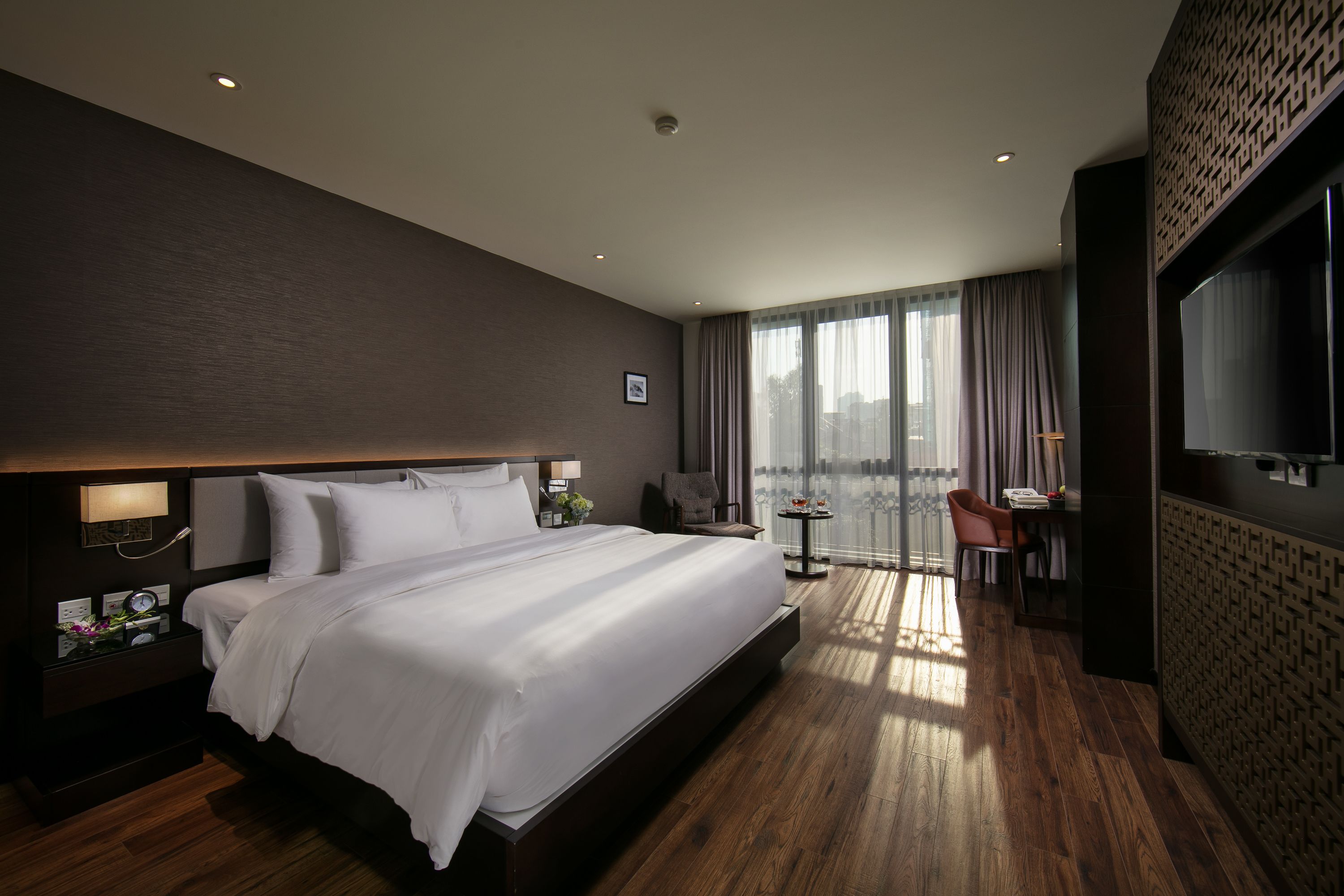 A modern hotel room with a large bed, a desk, a chair, and a TV.