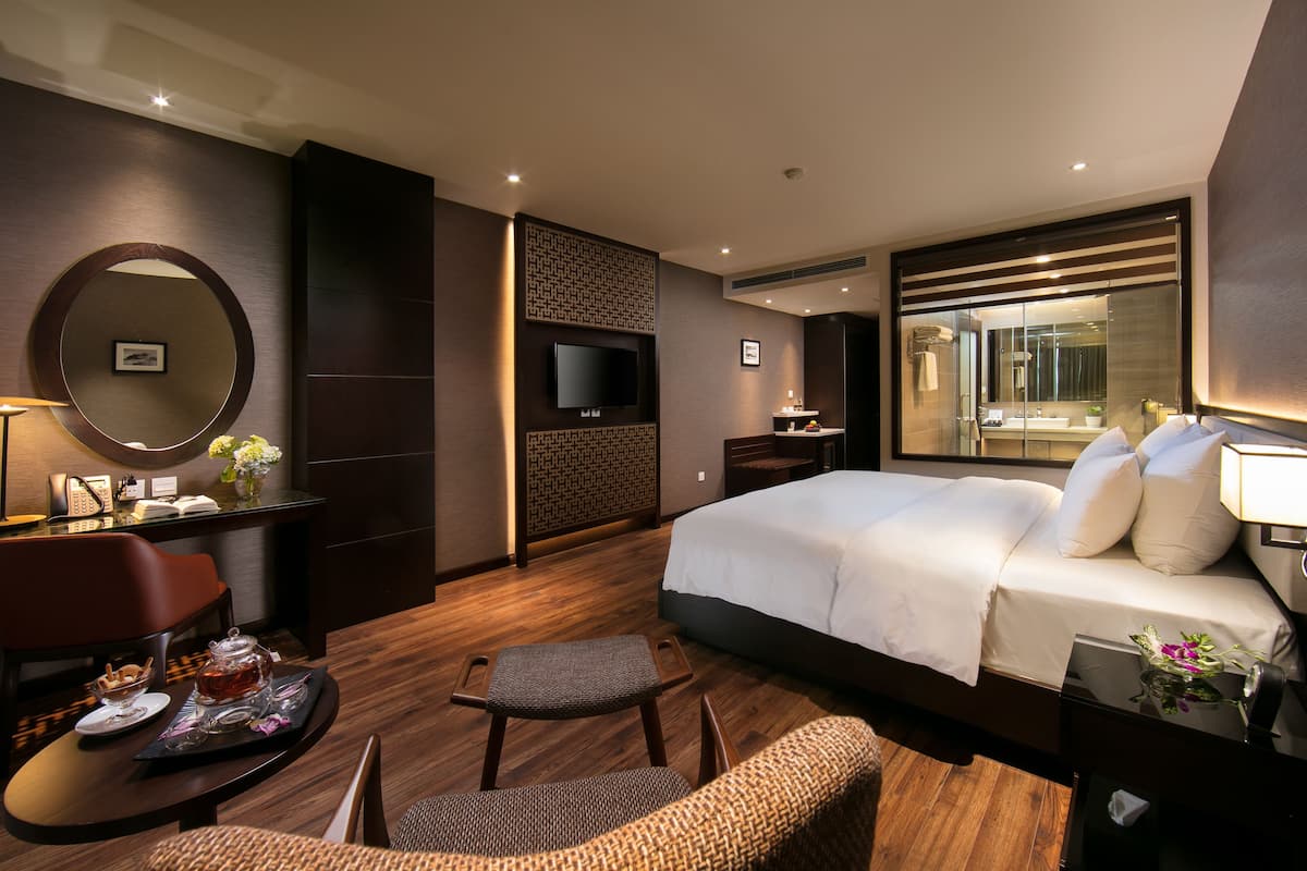 A hotel room with a large bed, a desk with a chair, a TV, and a bathroom with a mirror.