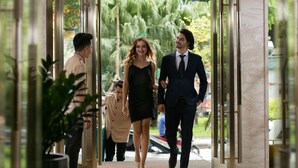 Entrada de hotel con puerta de vidrio, un hombre y una mujer caminando adentro y una persona con uniforme cerca.