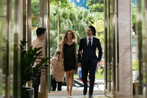 A hotel entrance with a glass door, a man and a woman walking through, and a person in a uniform standing nearby.