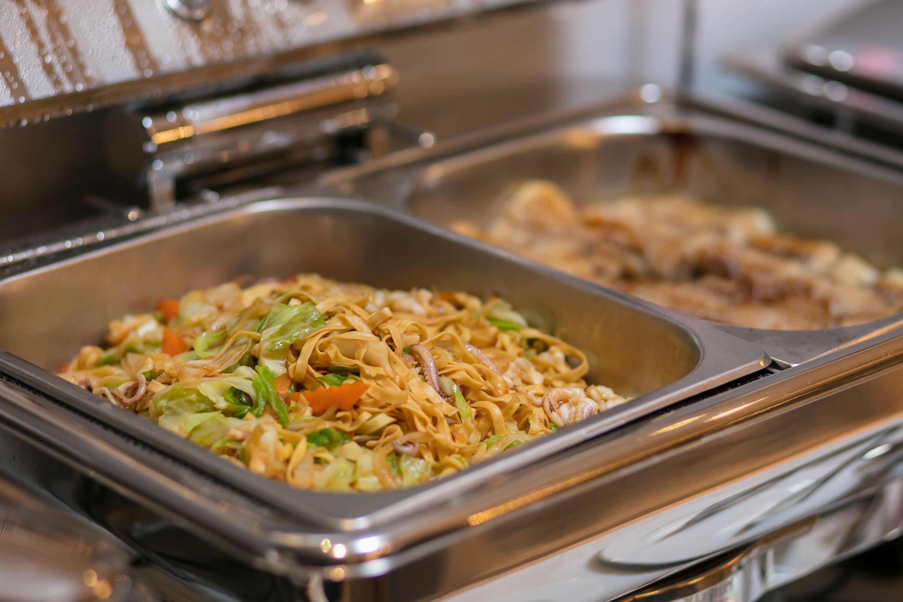 Un bufé con diversos platos, incluyendo fideos y verduras.
