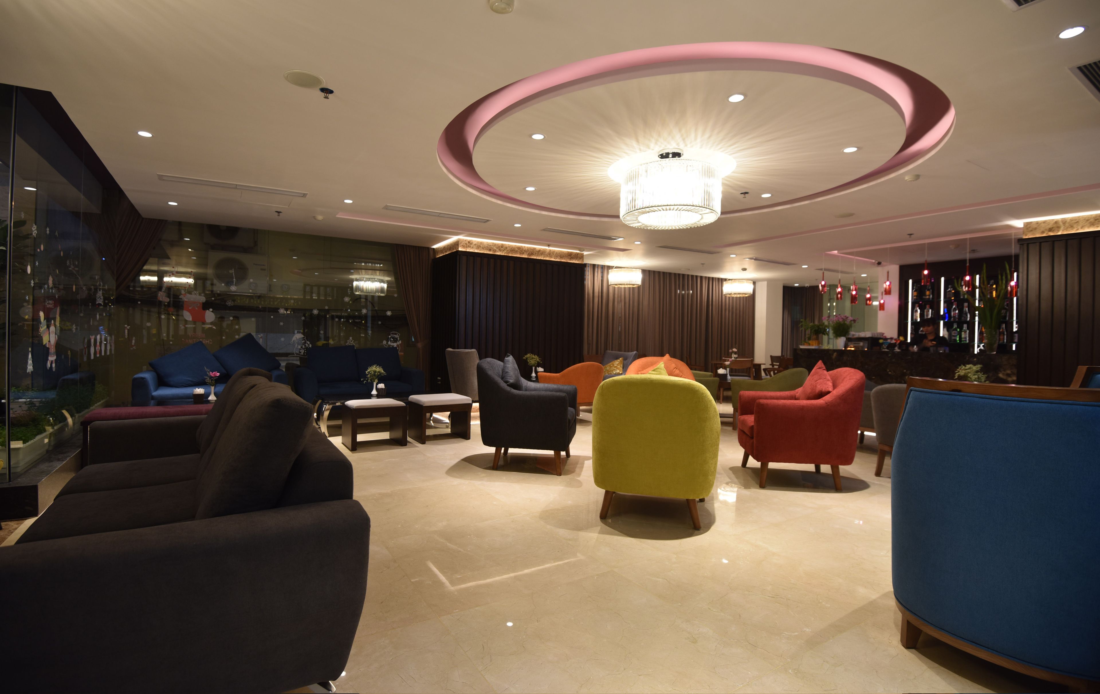 Un espace lounge moderne offrant divers types de sièges, notamment des canapés et des fauteuils, un bar avec des bouteilles exposées et un grand lustre.